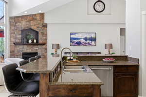 Kitchen with dark stone countertops, open floor plan, dishwasher, a stone fireplace, and vaulted ceiling