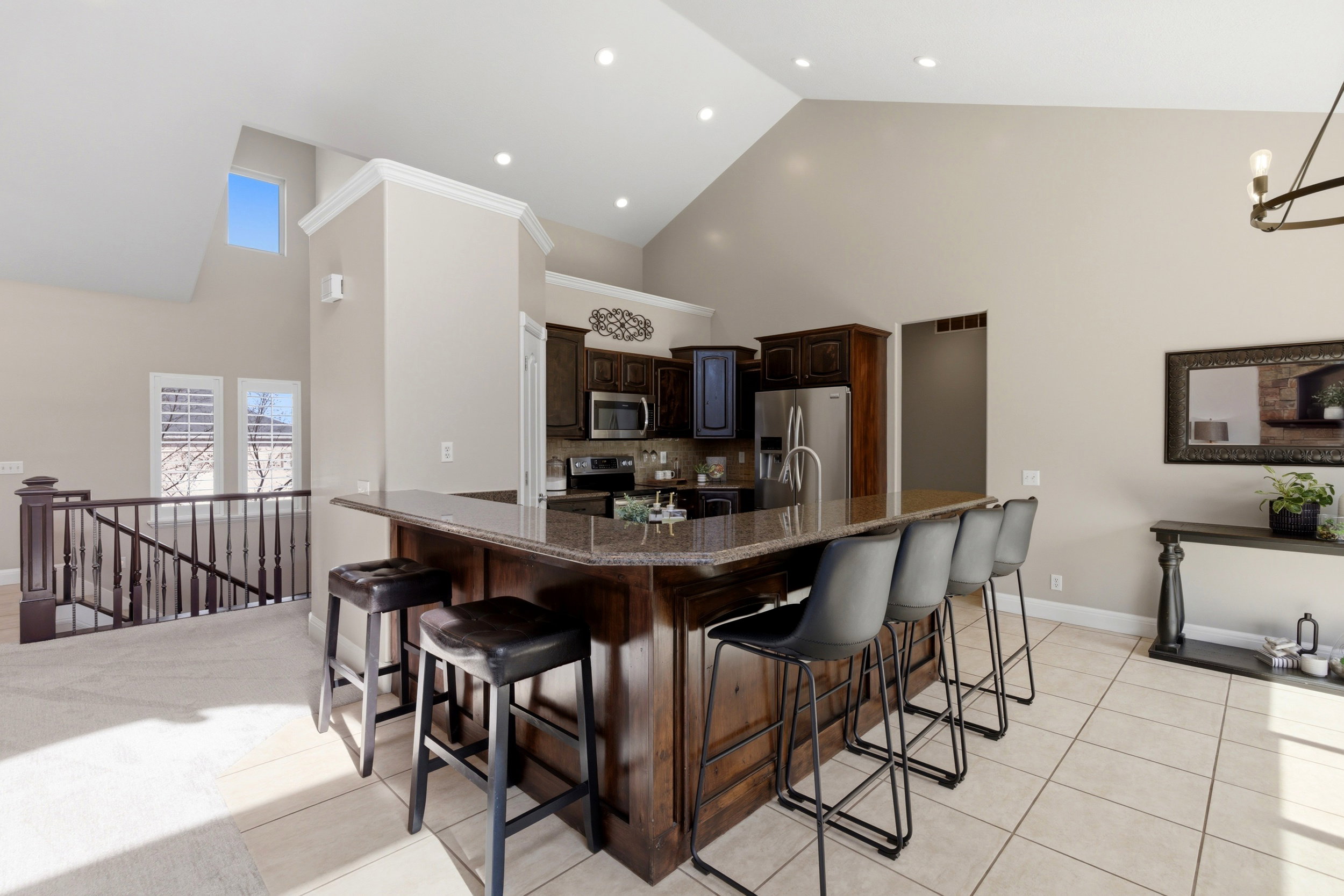 Kitchen featuring dark wood finish cabinetry, a kitchen bar, dark stone counters, stainless steel appliances, and lofted ceiling