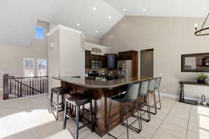 Kitchen featuring dark wood finish cabinetry, a kitchen bar, dark stone counters, stainless steel appliances, and lofted ceiling