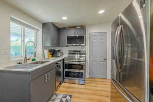 Kitchen with gray cabinetry, stainless steel appliances, light wood-type flooring, recessed lighting, and a textured ceiling