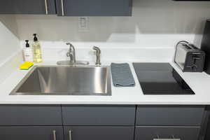 Kitchen view of black electric stovetop, gray cabinetry, and light stone counters