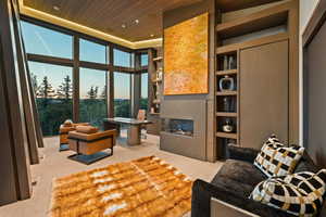 Living room featuring expansive windows, a high wood ceiling, a glass covered fireplace, light colored carpet, and recessed lighting