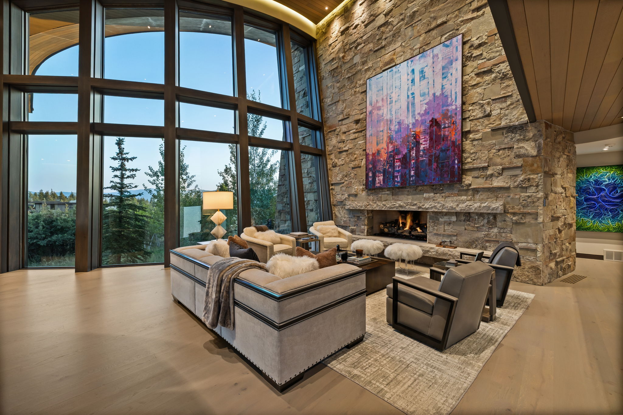Living room with a high wooden ceiling, a stone fireplace, wood finished floors, and floor to ceiling windows