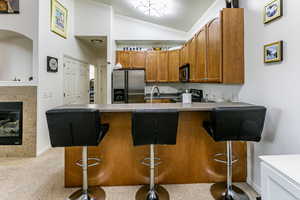 Kitchen with wood finish cabinets, stainless steel appliances, light countertops, a tiled fireplace, and vaulted ceiling