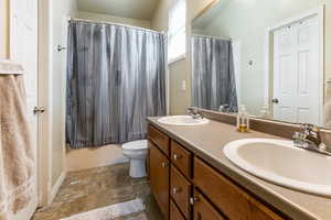 Full bathroom featuring double vanity, stone finish floors, and shower / bath combination with curtain