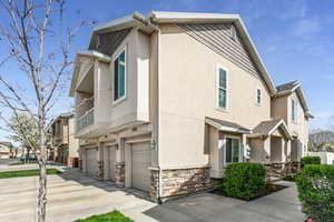 View of side of property with stucco siding, an attached garage, stone siding, and driveway