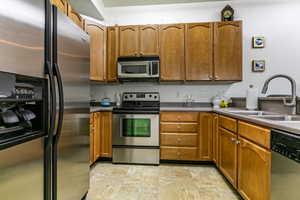 Kitchen with stainless steel appliances, wood finish cabinets, dark countertops, and stone finish floors