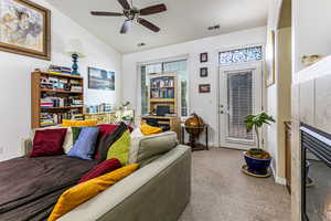 Carpeted living room with vaulted ceiling, a tile fireplace, and ceiling fan