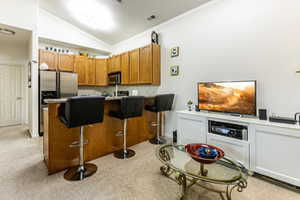 Kitchen featuring wood finish cabinets, stainless steel appliances, light countertops, light colored carpet, and lofted ceiling