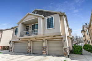 View of front of house featuring an attached garage, stucco siding, a balcony, and stone siding