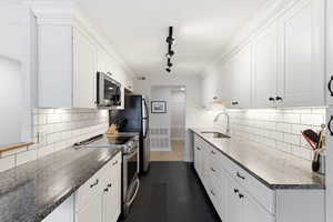 Kitchen with stainless steel appliances, white cabinets, track lighting, dark stone countertops, and dark slate tile patterned floors
