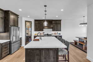 Spacious kitchen featuring an oversized island with countertop seating, stainless steel appliances, dark wood-finish cabinetry, and recessed lighting
