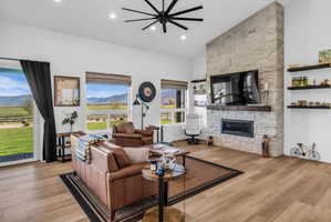 Spacious living area featuring a stone-clad fireplace with a wood mantel, wood-finish flooring, recessed lighting, and a modern ceiling fan