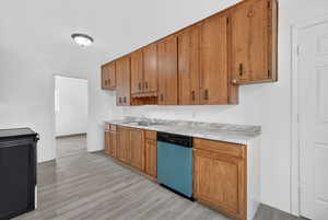 Kitchen with light countertops, wood finish cabinetry, dishwasher, light wood finished floors, and black range oven