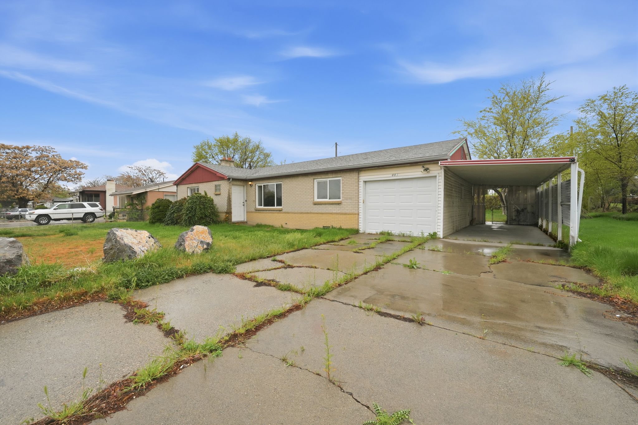 Ranch-style house featuring concrete driveway, an attached garage, a front lawn, brick siding, and a carport
