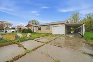 Ranch-style house featuring concrete driveway, an attached garage, a front lawn, brick siding, and a carport