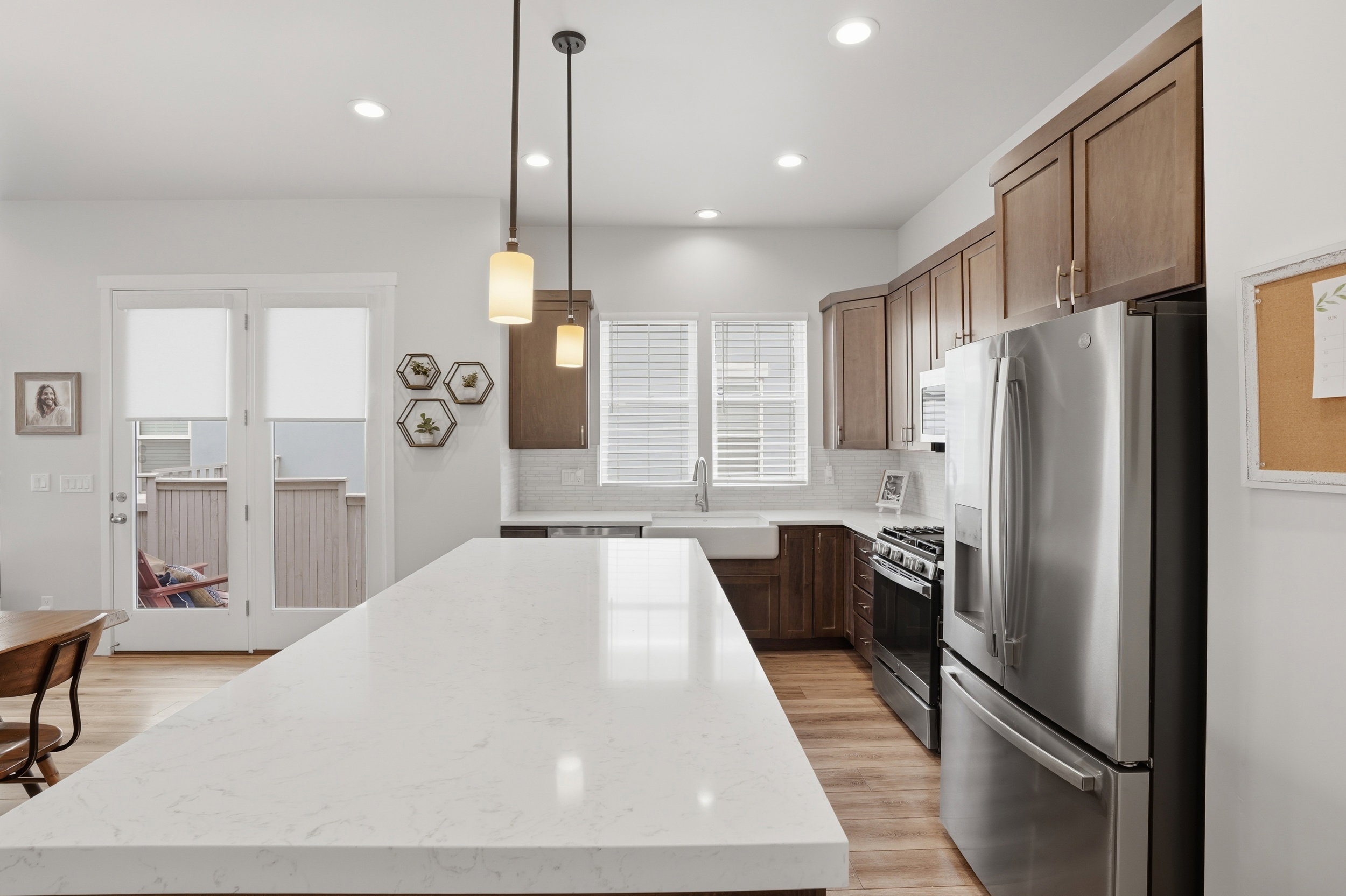 Kitchen featuring stainless steel appliances, decorative light fixtures, light stone counters, and plenty of natural light