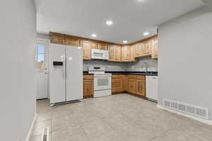 Kitchen featuring white appliances, dark countertops, light tile patterned floors, and recessed lighting
