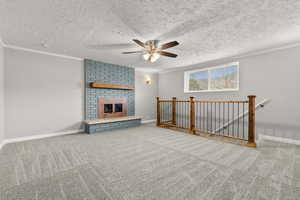 Unfurnished living room featuring carpet flooring, a fireplace, ceiling fan, a textured ceiling, and ornamental molding