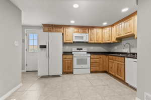 Kitchen with white appliances, recessed lighting, light tile patterned flooring, and dark stone countertops