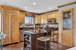 Kitchen with stainless steel appliances, a breakfast bar area, light wood finish cabinets, recessed lighting, and dark stone countertops
