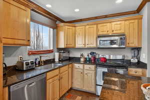 Kitchen featuring stainless steel appliances, dark stone countertops, ornamental molding, light wood finish cabinets, and recessed lighting