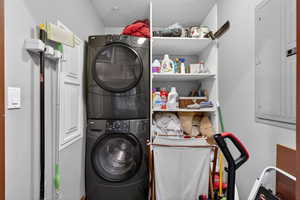Laundry area featuring electric panel, stacked washing machine and dryer, and a textured ceiling