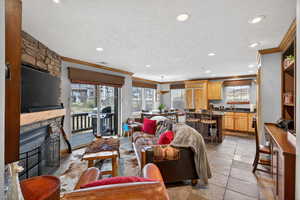 Living room featuring a stone fireplace, stone tile flooring, crown molding, a textured ceiling, and recessed lighting