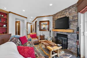 Living area with a stone fireplace, ornamental molding, recessed lighting, and built in features