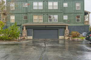 View of front facade with board and batten siding, an attached garage, asphalt driveway, and stone siding