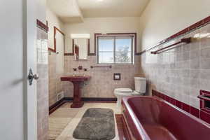 Full bath featuring a bath, light tile patterned floors, wainscoting, and tile walls