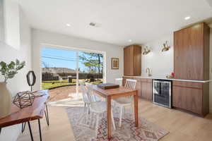 Dining room with beverage cooler, light wood-style floors, bar with sink, and recessed lighting