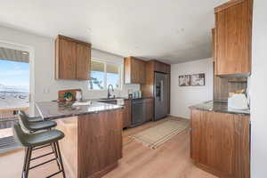 Kitchen featuring dark stone countertops, wood finish cabinetry, a peninsula, and light wood-type flooring