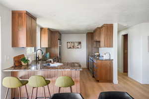 Kitchen featuring wood finish cabinets, dark stone counters, light wood-style flooring, and stainless steel appliances