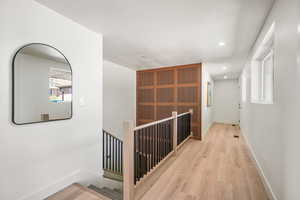Hall with light wood-style floors, an upstairs landing, and recessed lighting