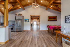 Dining area featuring light wood-type flooring, suspended lighting, and a high wood beamed ceiling