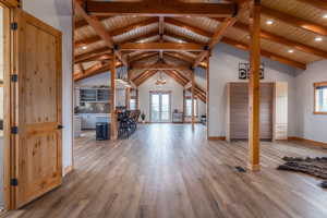 Unfurnished living room with hanging lights, light wood-type flooring, and a high wooden beamed ceiling