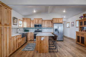 Kitchen with stainless steel appliances, light wood-style flooring, a kitchen island, a kitchen bar, and tasteful backsplash