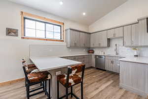 Kitchen with a peninsula, vaulted ceiling, a breakfast bar area, backsplash, and light wood finished floors
