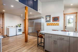 Kitchen with a breakfast bar area, high quality fridge, recessed lighting, separate washer and dryer, and light wood finished floors