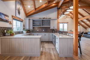 Kitchen featuring a peninsula, light wood finished floors, a high wooden beamed ceiling, decorative backsplash, and light stone counters