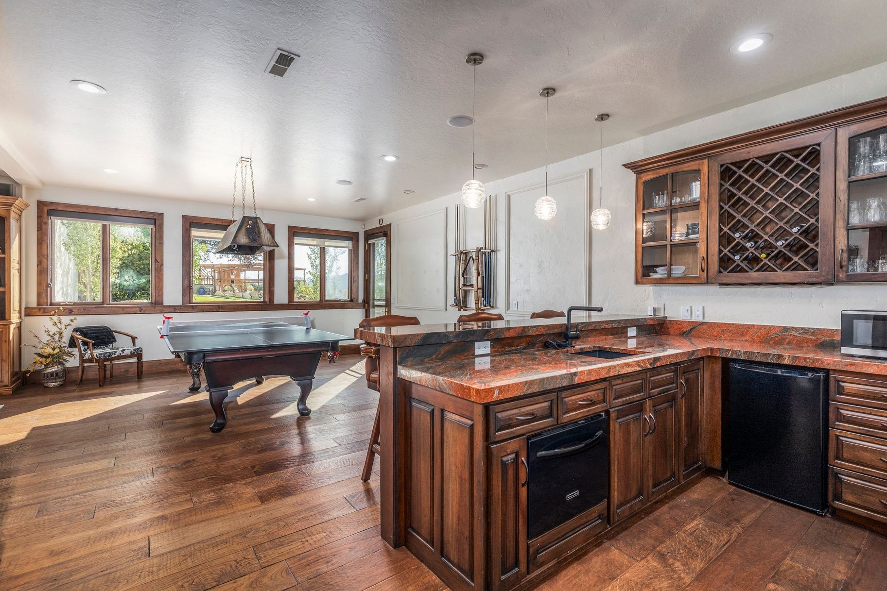 Indoor wet bar featuring glass insert cabinets, dark wood finish cabinetry, black appliances, dark wood-style flooring, and decorative light fixtures