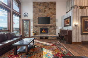 Living room with a stone fireplace, dark wood finished floors, and a high ceiling