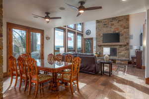 Dining space with hardwood / wood-style flooring, healthy amount of natural light, a stone fireplace, and a ceiling fan