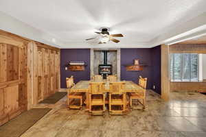 Dining area featuring a wood stove, a ceiling fan, and a textured ceiling