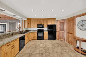 Kitchen featuring light stone countertops, black appliances, light wood finish cabinetry, and recessed lighting