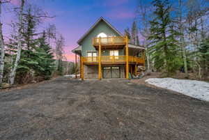 Chalet / cabin with a wooden deck, driveway, stone siding, a garage, and stucco siding