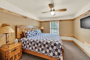 Bedroom featuring wallpapered walls, ceiling fan, dark carpet, and a textured ceiling