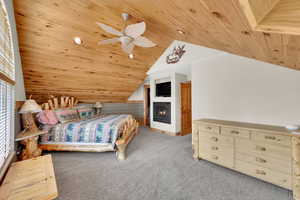 Carpeted bedroom with wood ceiling, ceiling fan, recessed lighting, and a warm lit fireplace