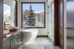 Full bath featuring a soaking tub, vanity, light marble finish flooring, a marble finish shower, and healthy amount of natural light